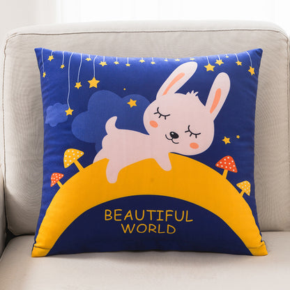 Decorative pillow with a cartoon rabbit on a blue background, featuring stars and the text 'Beautiful World' on a beige couch.