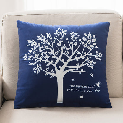 Navy blue pillow with white tree design and text on a beige couch